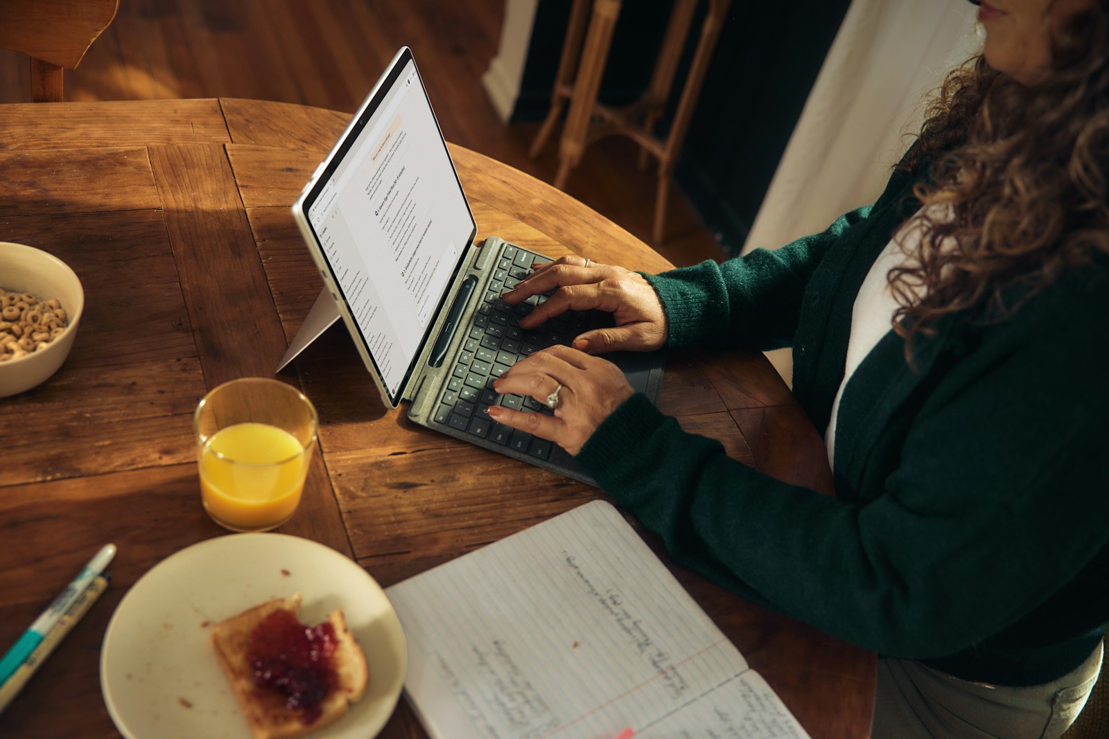 Une femme tape sur son ordinateur portable à une table en bois, en prenant son petit-déjeuner.