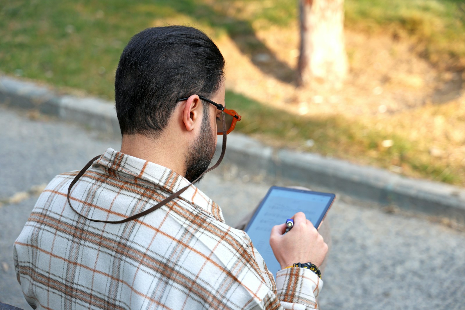Man in plaid shirt reading tablet outdoors