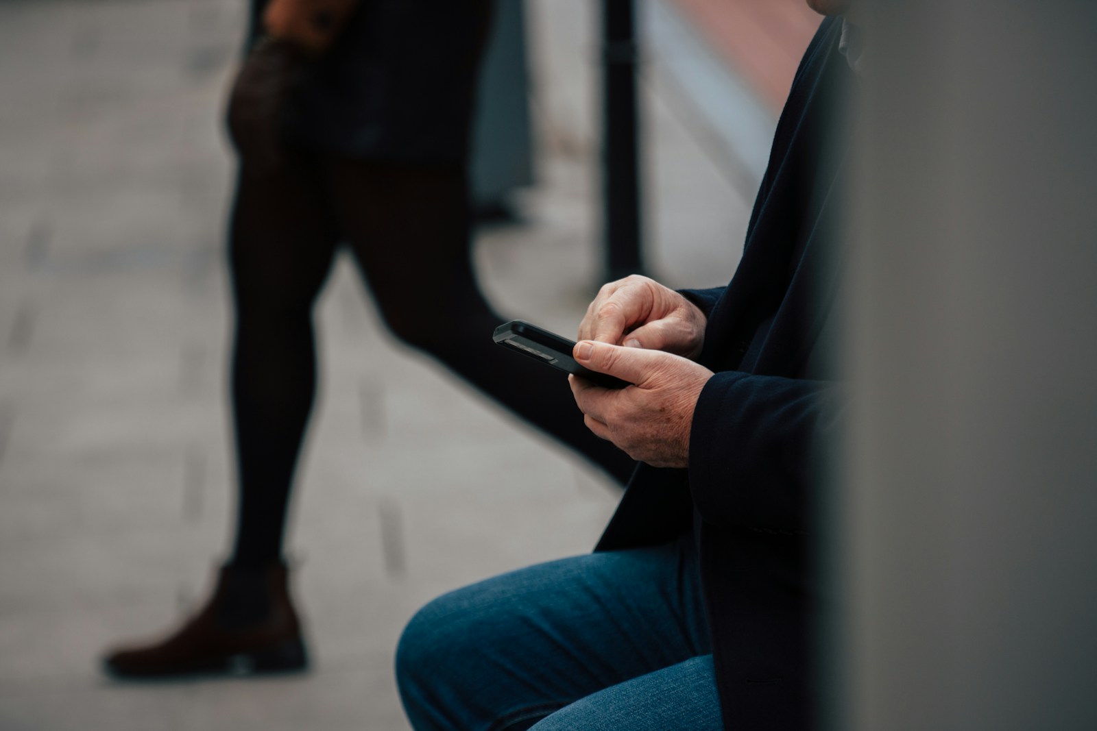 Man using smartphone while person walks by