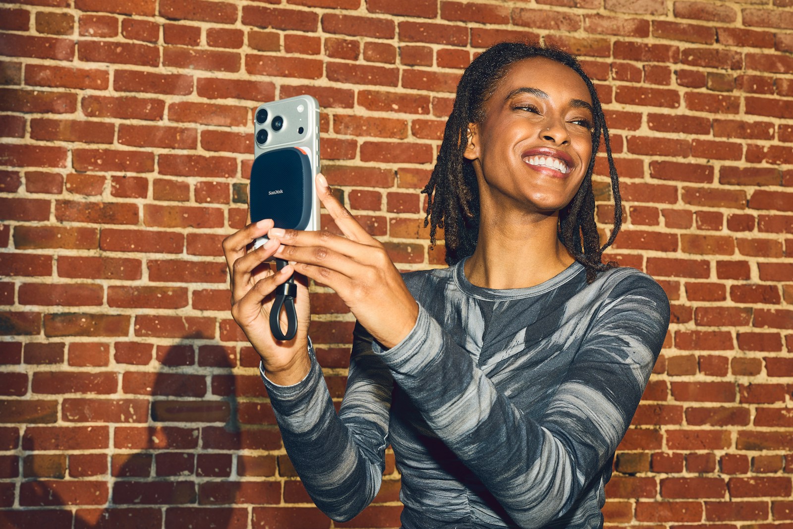 Smiling woman takes a selfie with smartphone against brick wall.